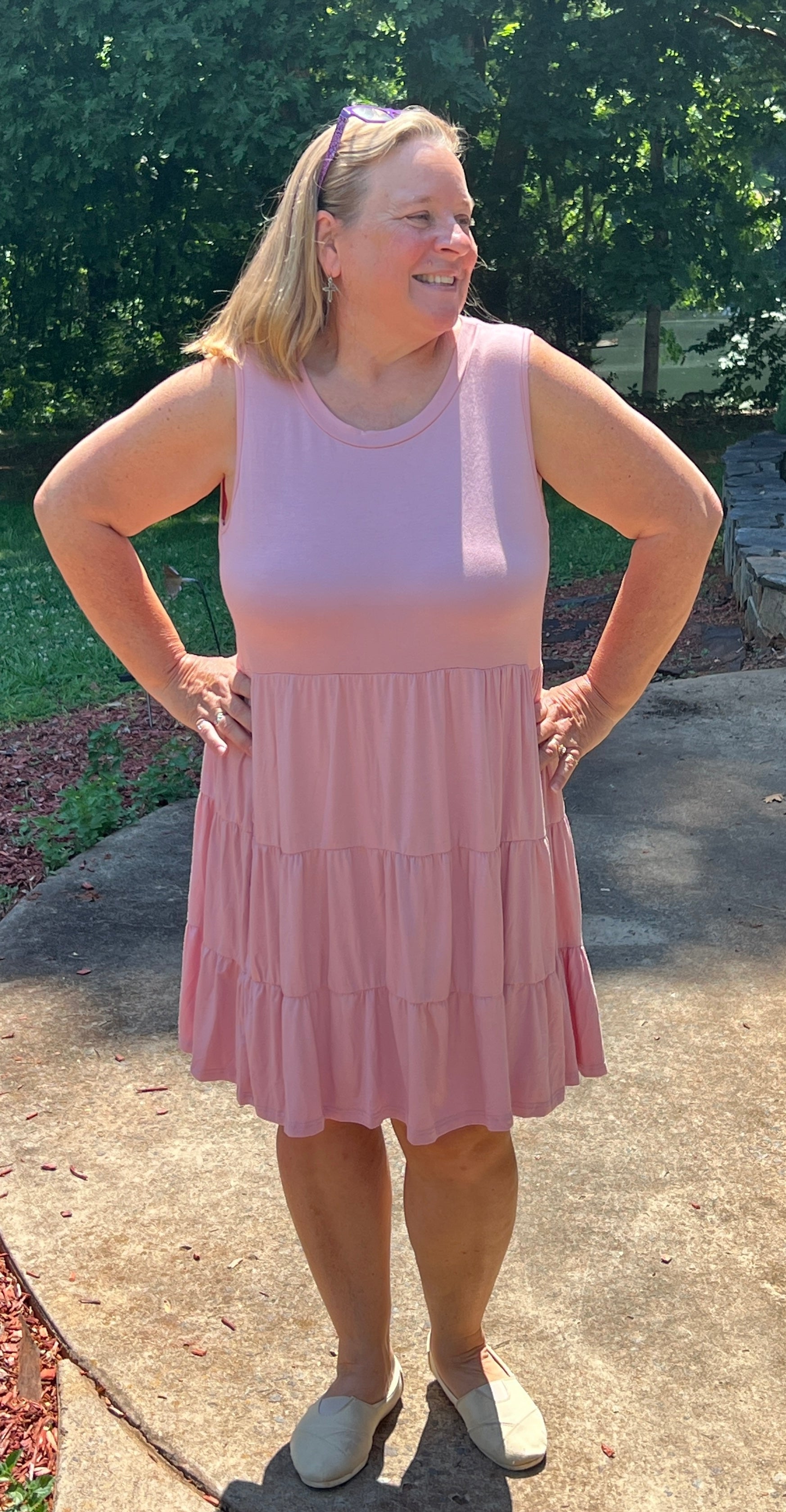 Soft, silky feel plus size baby doll midi dress is pale rose pink in color. It has a plain bodice with round neckline, is sleeveless, and has a tiered skirt. In 1X-3X